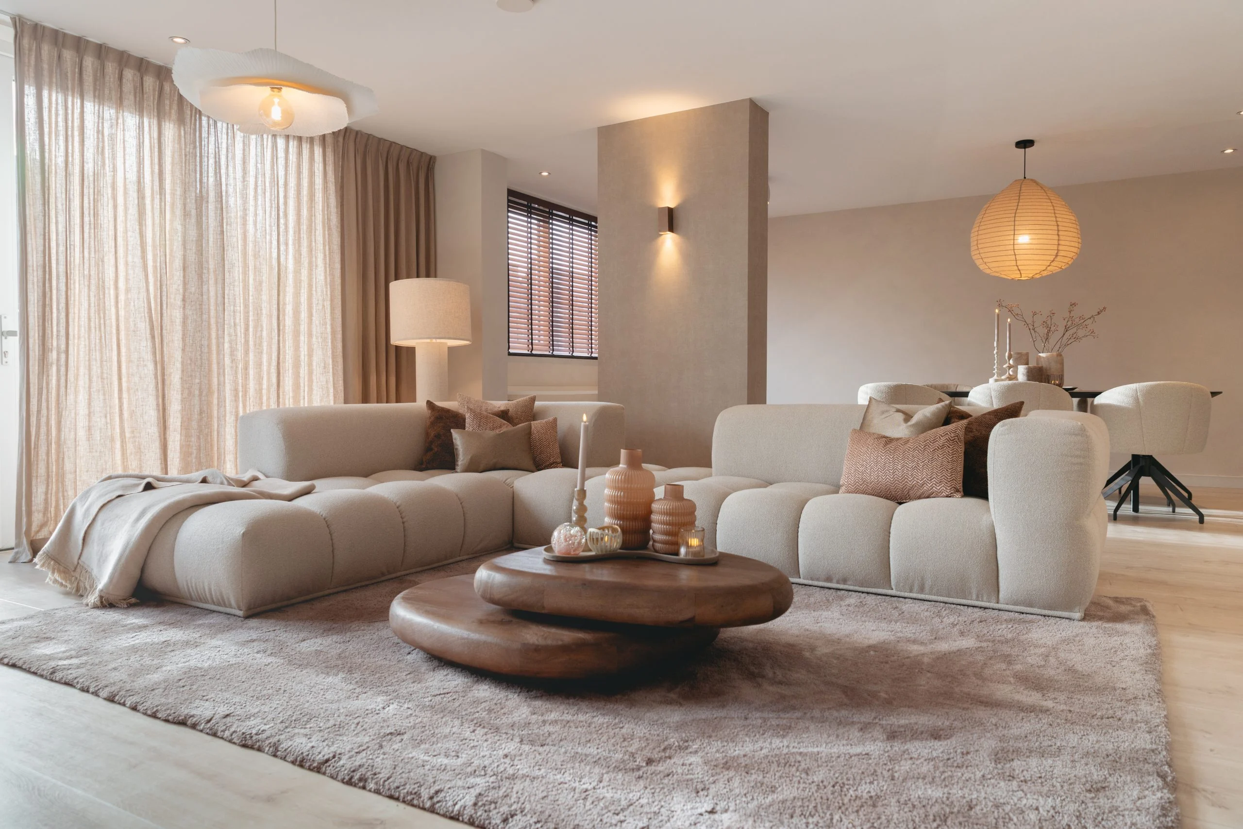 Warme woonkamer met een modulaire Oriane hoekbank in crème boucle, ronde houten salontafels en zachte linnen accenten
