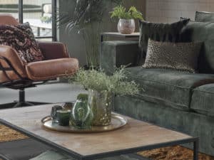 Bank Annabelle in een groene velvet stof met een okergeel vloerkleed en cognac fauteuil