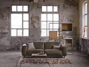 Grijze velvet bank in een industrieel en rustig interieur met een groot vloerkleed.