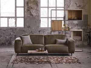 Grijze velvet bank in een industrieel en rustig interieur met een groot vloerkleed.