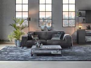Grijze velvet bank in een industrieel en rustig interieur met een groot vloerkleed.