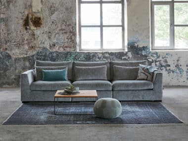 Brede bank met comfortabele zittingen. Blauw/grijze stof en een groot vloerkleed.
