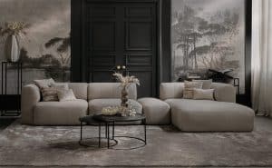 Elementenbank Emanuelle met een longchair en een hocker tussen de elementen in. Uitgevoerd in een lichte beige stof. Gecombineerd met een groot vloerkleed en naturel decoratie.