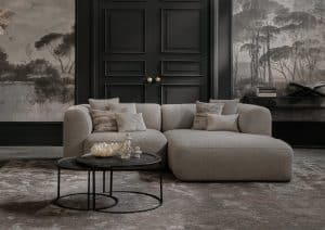 Compacte elementenbank Emanuelle uitgevoerd in een beige stof. Gestyled met naturel en zwarte decoratie en panelen met behang aan de wand.