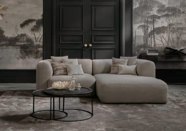 Compacte elementenbank Emanuelle uitgevoerd in een beige stof. Gestyled met naturel en zwarte decoratie en panelen met behang aan de wand.