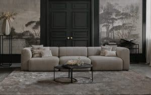 Bank emanuelle met 3 zittingen. Uitgevoerd in een beige stof. Gestyled met een vloerkleed en naturel en zwarte decoratie.