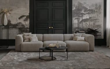Bank emanuelle met 3 zittingen. Uitgevoerd in een beige stof. Gestyled met een vloerkleed en naturel en zwarte decoratie.