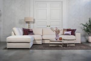 Beige hoekbank met grote hoek, gestyled met woonaccessoires in Burgundy.