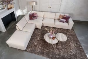 Beige hoekbank met grote hoek, gestyled met woonaccessoires in Burgundy.