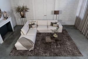 Lichte beige hoekbank met bruine woonaccessoires.
