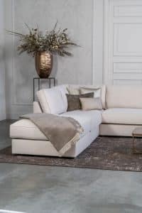 Lichte beige hoekbank met bruine woonaccessoires.