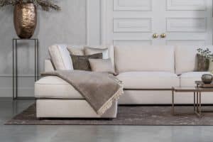 Lichte beige hoekbank met bruine woonaccessoires.