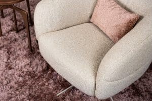 Levi draaifauteuil van Gusj in lichte bouclé stof met draaionderstel op een roze rond vloerkleed in een stijlvol interieur.
