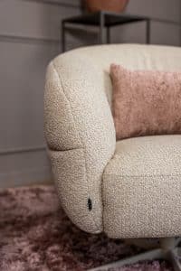 Levi draaifauteuil van Gusj in lichte bouclé stof met draaionderstel op een roze rond vloerkleed in een stijlvol interieur.