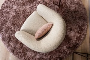 Levi draaifauteuil van Gusj in lichte bouclé stof met draaionderstel op een roze rond vloerkleed in een stijlvol interieur.