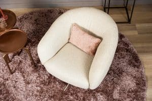 Levi draaifauteuil van Gusj in lichte bouclé stof met draaionderstel op een roze rond vloerkleed in een stijlvol interieur.