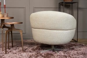 Levi draaifauteuil van Gusj in lichte bouclé stof met draaionderstel op een roze rond vloerkleed in een stijlvol interieur.