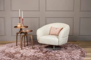 Levi draaifauteuil van Gusj in lichte bouclé stof met draaionderstel op een roze rond vloerkleed in een stijlvol interieur.