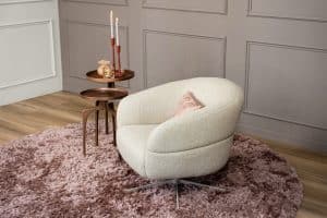 Levi draaifauteuil van Gusj in lichte bouclé stof met draaionderstel op een roze rond vloerkleed in een stijlvol interieur.