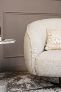 Lio draaifauteuil van Gusj in lichte bouclé stof met anodic brown draaionderstel op een rond vloerkleed in een warm interieur.