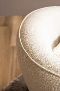 Lio draaifauteuil van Gusj in lichte bouclé stof met anodic brown draaionderstel op een rond vloerkleed in een warm interieur.