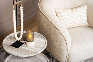Lio draaifauteuil van Gusj in lichte bouclé stof met anodic brown draaionderstel op een rond vloerkleed in een warm interieur.