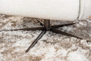 Lio draaifauteuil van Gusj in lichte bouclé stof met anodic brown draaionderstel op een rond vloerkleed in een warm interieur.