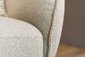 Lio draaifauteuil van Gusj in lichte bouclé stof met anodic brown draaionderstel op een rond vloerkleed in een warm interieur.