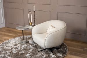 Lio draaifauteuil van Gusj in lichte bouclé stof met anodic brown draaionderstel op een rond vloerkleed in een warm interieur.