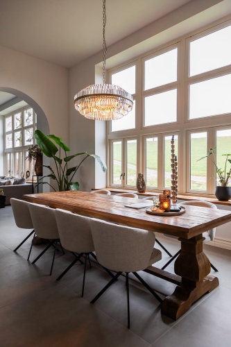 Lichtgrijze hoekbank Annabelle en houten eettafel met beige eetkamerstoelen in een rustiek interieur.