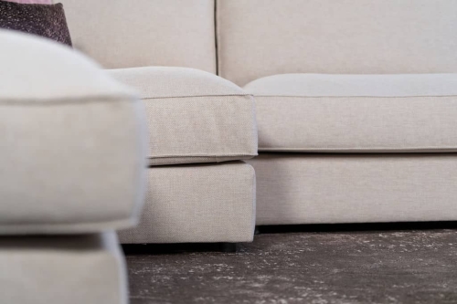 Beige hoekbank met grote hoek, gestyled met woonaccessoires in Burgundy.