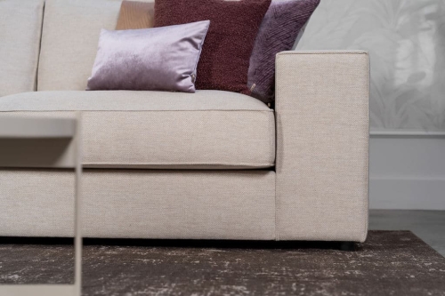 Beige hoekbank met grote hoek, gestyled met woonaccessoires in Burgundy.