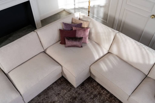 Beige hoekbank met grote hoek, gestyled met woonaccessoires in Burgundy.