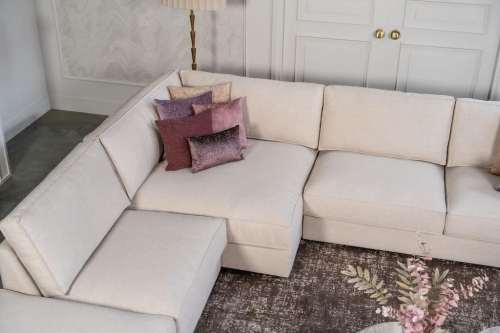 Beige hoekbank met grote hoek, gestyled met woonaccessoires in Burgundy.